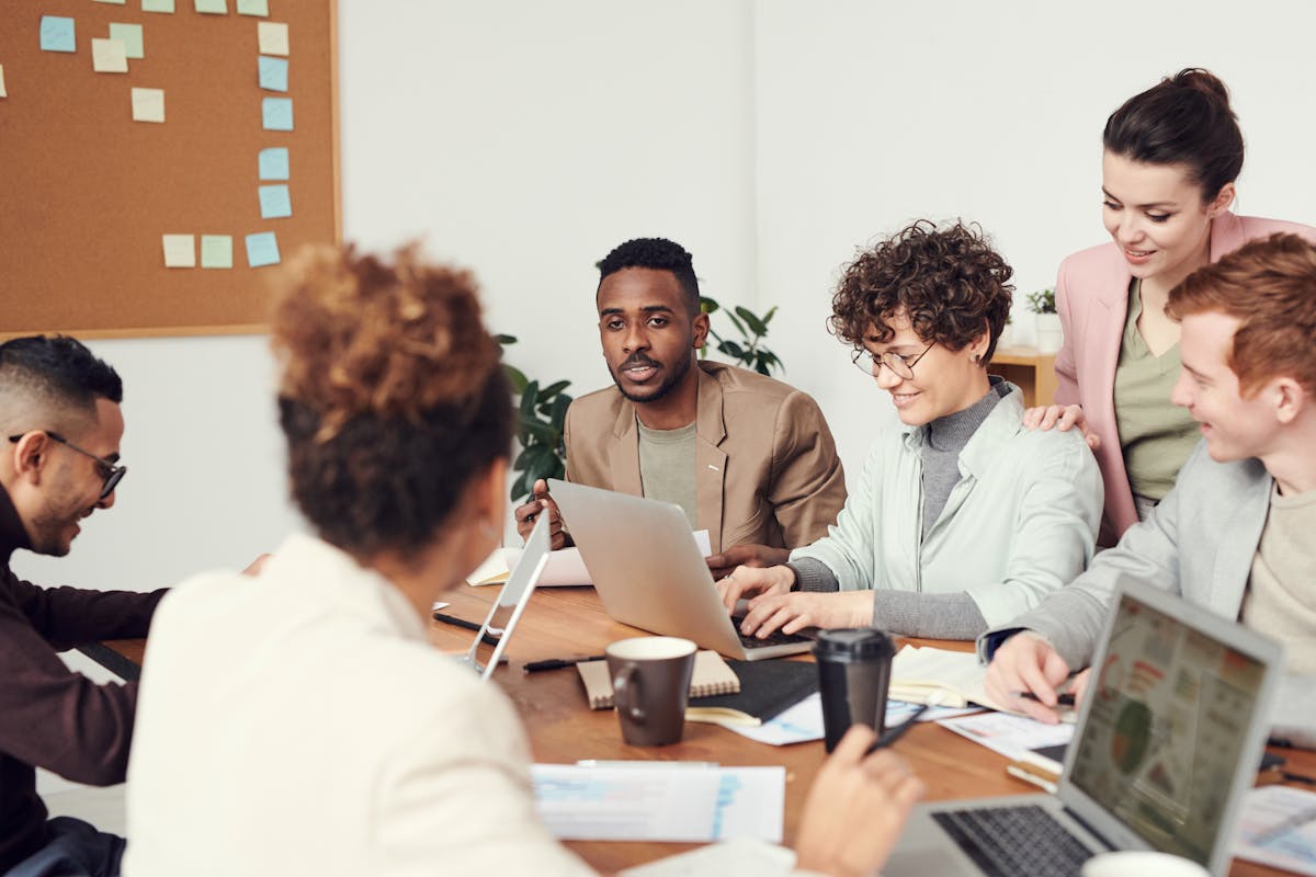 Diverse team collaborating around a table with laptops and documents in a modern office setting.